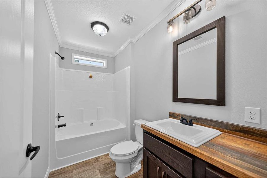 Bathroom with ornamental molding, shower / bathtub combination, vanity, light wood finished floors, and a textured ceiling Bathroom with ornamental molding, shower / bathtub combination, vanity, light wood finished floors, and a textured ceiling
