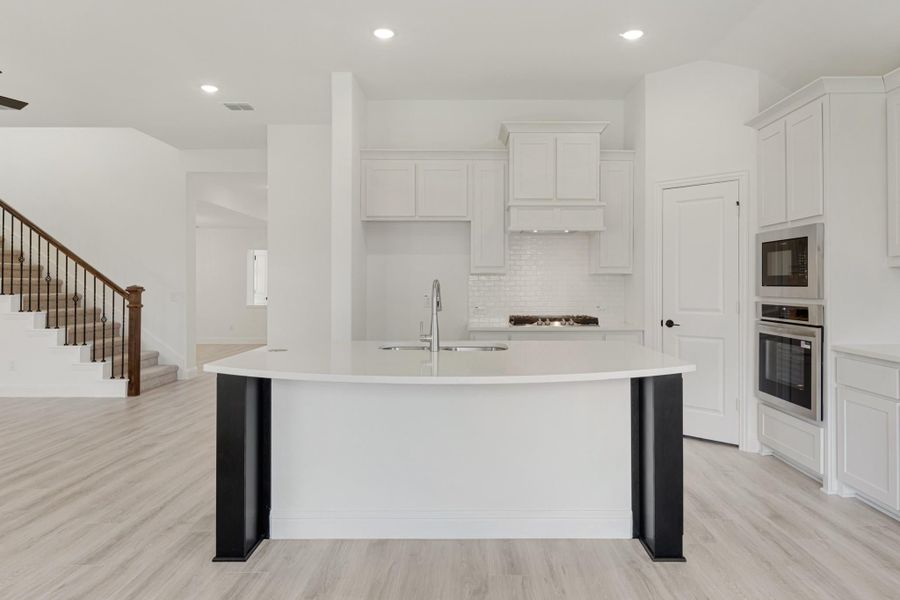 White kitchen with large curved island, white cabinets, stainless steel double ovens, and light wood floors