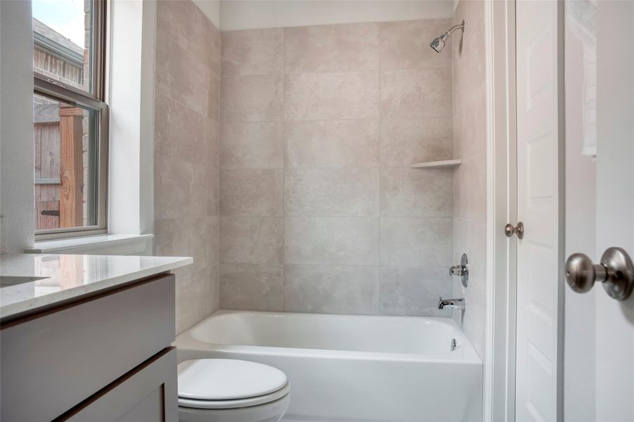 Bright bathroom with a large window, featuring a bathtub and shower, beige tiled walls, and a sleek countertop. Bright bathroom with a large window, featuring a bathtub and shower, beige tiled walls, and a sleek countertop.