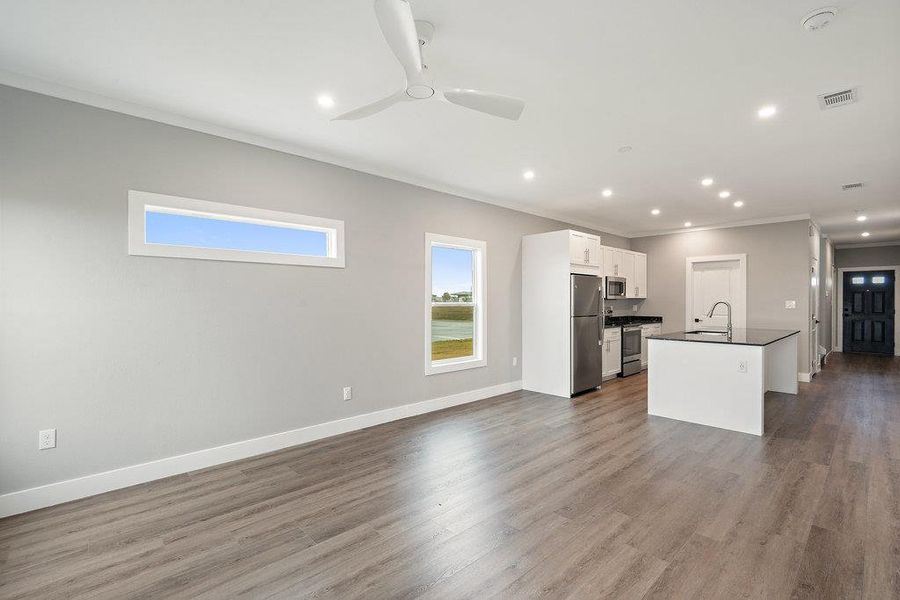 Kitchen with open floor plan, white cabinetry, crown molding, appliances with stainless steel finishes, and dark countertops