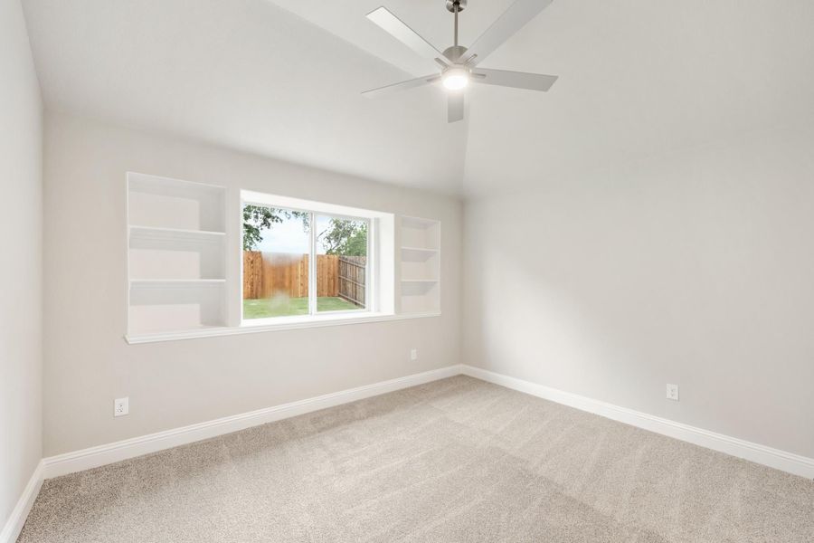 Empty bedroom with vaulted ceiling, ceiling fan, built-in shelves, and carpet flooring