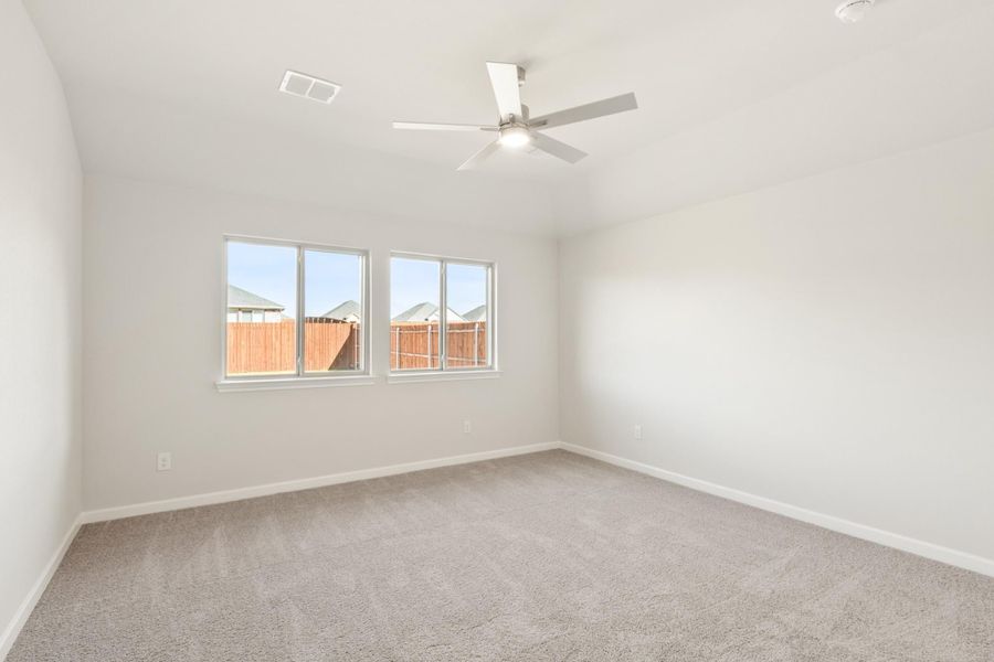 Empty bedroom with gray carpet, ceiling fan, and triple window overlooking backyard fence Empty bedroom with gray carpet, ceiling fan, and triple window overlooking backyard fence