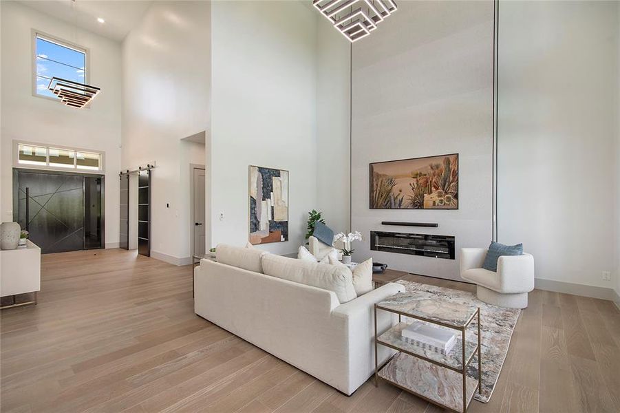 Living room with light wood finished floors, a towering ceiling, and a barn door