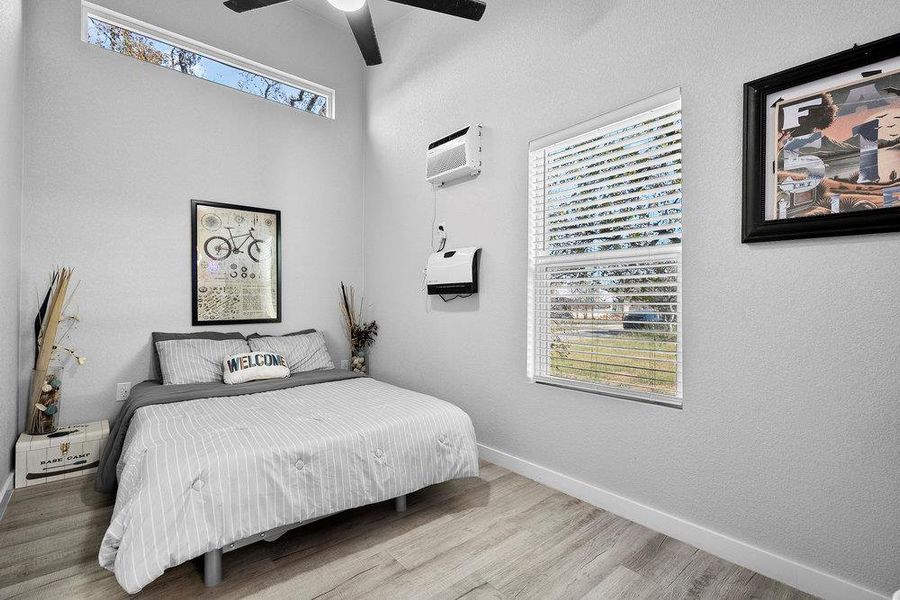 Bedroom featuring wood finished floors, ceiling fan, and a wall mounted AC.