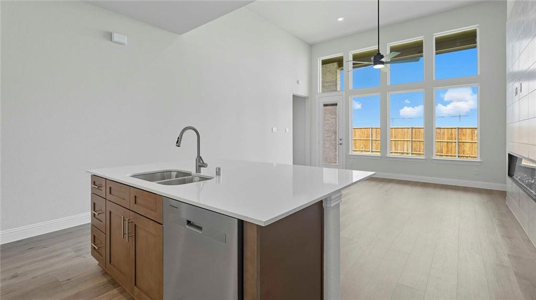 Kitchen with stainless steel dishwasher, light wood-type flooring, an island with sink, a high ceiling, and light stone countertops