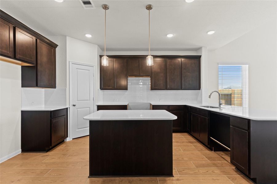 Impressive view of the gourmet kitchen featuring granite countertops, beautiful cabinetry, stainless steel appliances, and a spacious island with breakfast bar seating. The open design allows the kitchen to flow effortlessly into the dining and family areas, all accented by the elegant wood looking tile flooring throughout the main living areas.