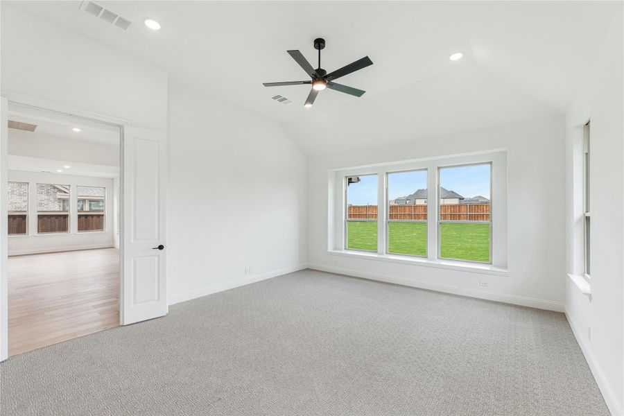 Empty bedroom with vaulted ceiling, ceiling fan, carpet flooring, and large windows overlooking backyard