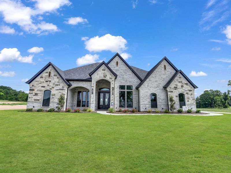French country home with a front lawn, roof with shingles, brick siding, and stone siding French country home with a front lawn, roof with shingles, brick siding, and stone siding