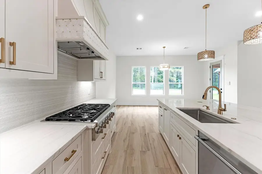 Bright and modern kitchen featuring light cabinetry, a spacious island with a sink, sleek gas stove, and elegant pendant lighting. Large windows offer natural light and views of the outdoor area.