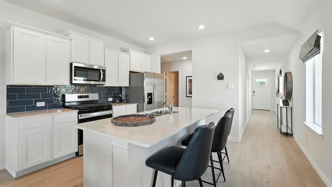 Kitchen featuring appliances with stainless steel finishes, white cabinets, an island with sink, decorative backsplash, and light wood-style floors