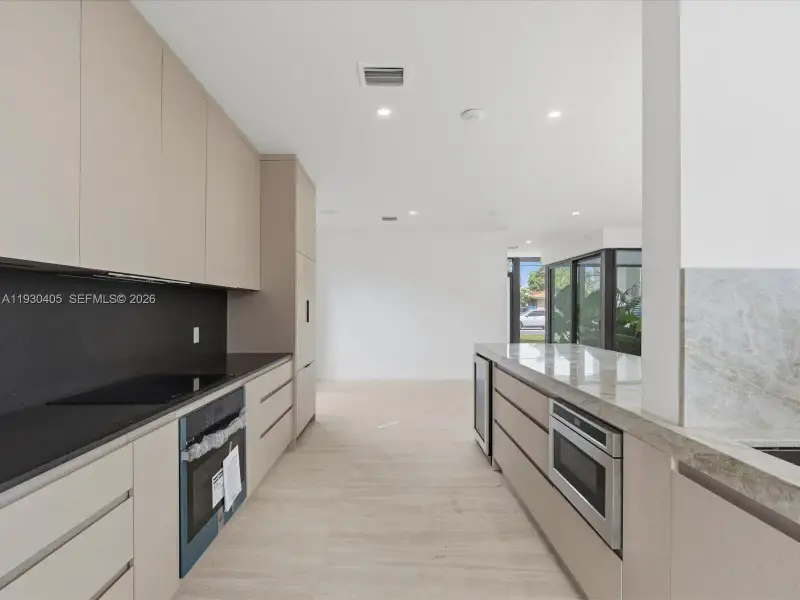 Modern kitchen featuring light-toned slab cabinetry, solid-surface countertops, recessed ceiling lighting, and built-in stainless steel appliances Modern kitchen featuring light-toned slab cabinetry, solid-surface countertops, recessed ceiling lighting, and built-in stainless steel appliances
