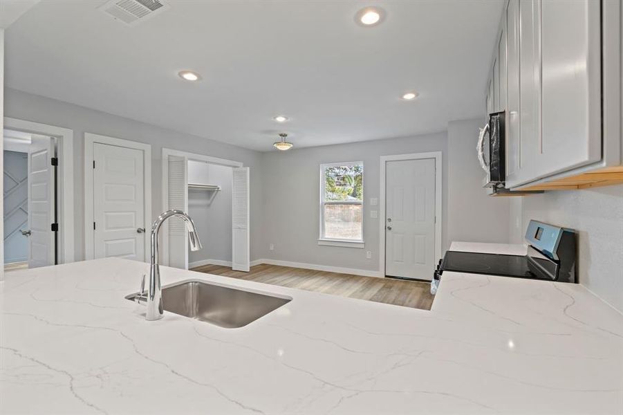 Kitchen featuring light stone counters, sink, range with electric stovetop, and light wood-type flooring