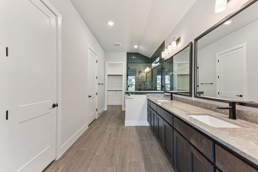 Full bath featuring double vanity, light wood-style floors, vaulted ceiling, recessed lighting, and a walk in closet Full bath featuring double vanity, light wood-style floors, vaulted ceiling, recessed lighting, and a walk in closet