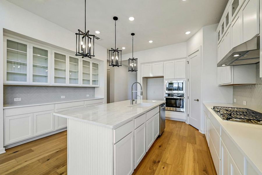 Kitchen with appliances with stainless steel finishes, a chandelier, under cabinet range hood, backsplash, and light wood-style floors