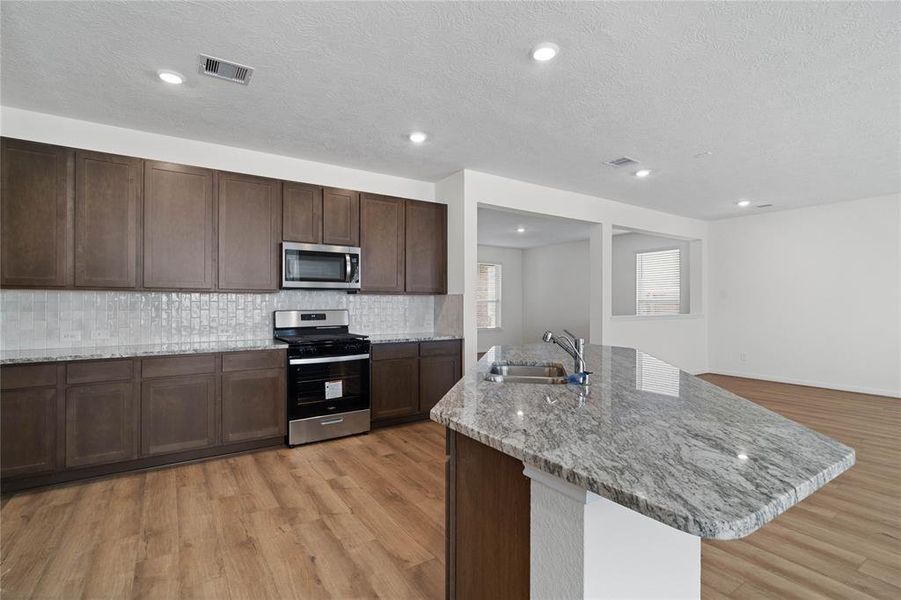 This stunning kitchen displays such a beautiful contrast with the dark stained cabinets, neutral paint, granite countertops, modern tile backsplash, SS appliances, breakfast bar, recessed lighting, high ceilings and walk in pantry.