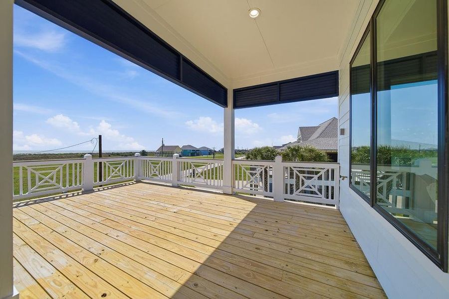 This photo showcases a spacious, covered wooden deck with white railing, offering scenic views of the surrounding neighborhood and open skies, perfect for outdoor relaxation.