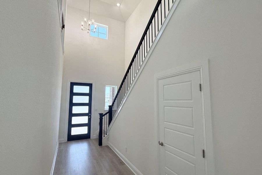 Foyer featuring a high vaulted ceiling, wood-finish flooring, a contemporary chandelier, a modern front entry door with privacy glass, and a staircase with an open black iron railing