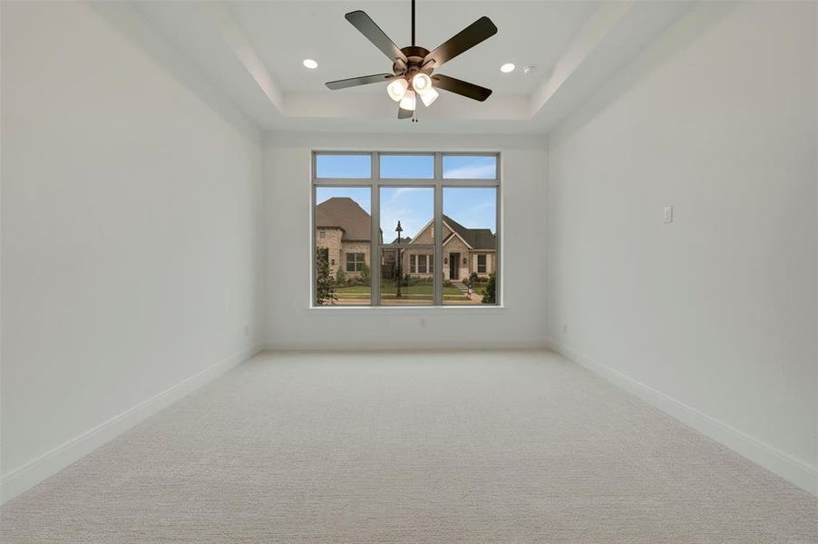 Spacious room featuring a tray ceiling with recessed lighting, a modern ceiling fan, large windows, plush carpeting, and crisp white baseboards