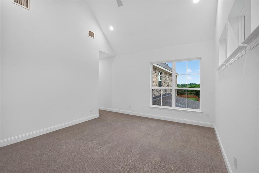 Vaulted ceiling room featuring neutral carpeting, white walls, recessed lighting, and a window overlooking a paved outdoor area and distant greenery Vaulted ceiling room featuring neutral carpeting, white walls, recessed lighting, and a window overlooking a paved outdoor area and distant greenery