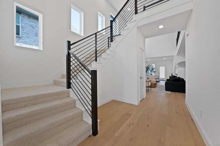 Two-story foyer featuring light wood-finish flooring, a contemporary staircase with black metal balusters, and a carpeted stairway with white risers