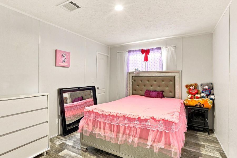 Recessed lighting illuminates wood-look flooring and clean white walls in this cozy bedroom.