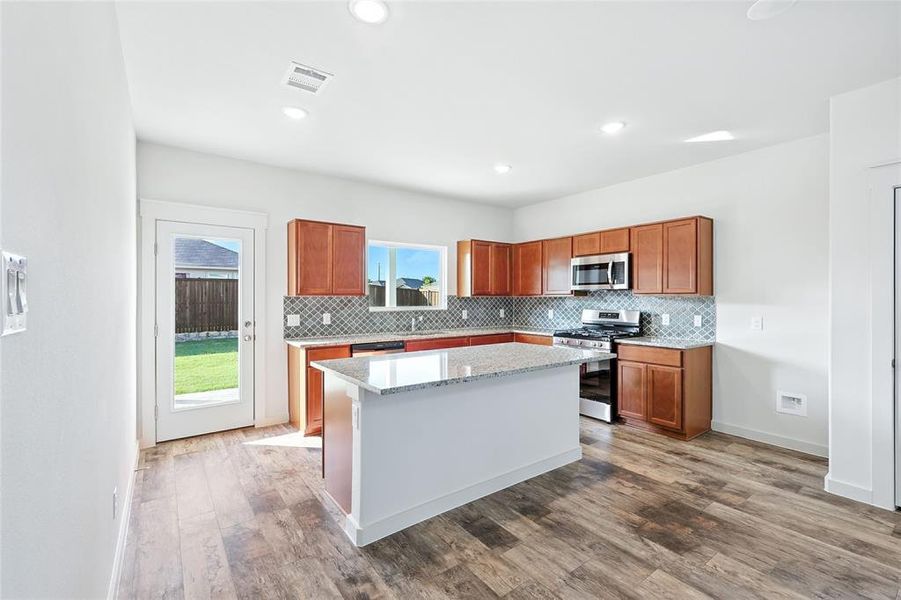 Kitchen featuring backsplash, brown cabinetry, light stone countertops, stainless steel appliances, and recessed lighting Kitchen featuring backsplash, brown cabinetry, light stone countertops, stainless steel appliances, and recessed lighting