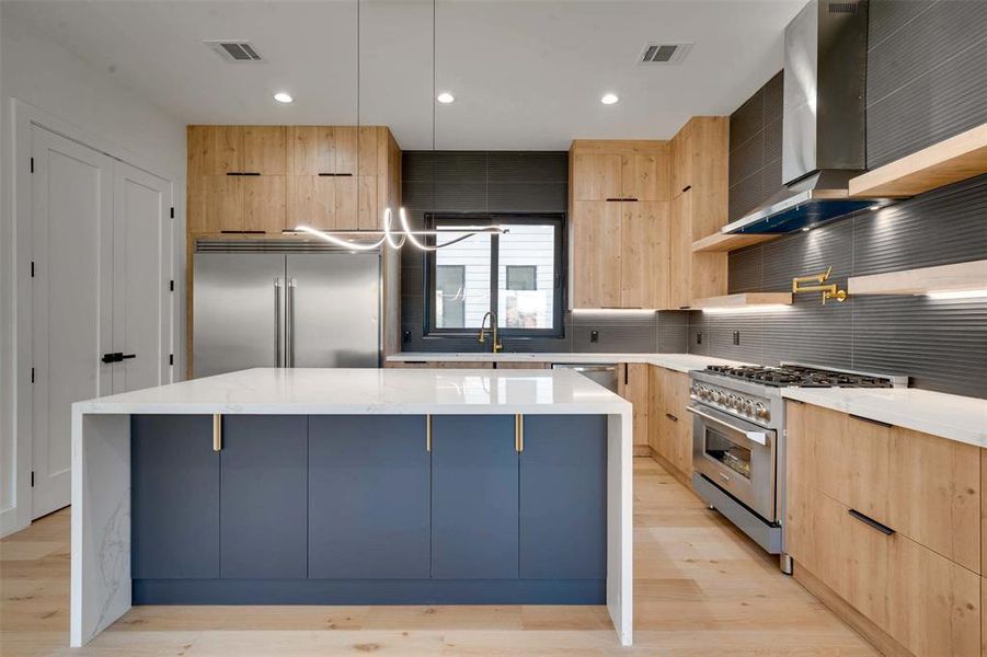 Kitchen featuring high quality appliances, a center island, light hardwood / wood-style floors, and wall chimney range hood