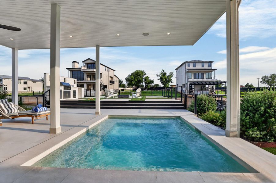 An inviting private pool beckons beneath a covered patio, overlooking a meticulously landscaped yard with a fire pit and distant modern residences. An inviting private pool beckons beneath a covered patio, overlooking a meticulously landscaped yard with a fire pit and distant modern residences.