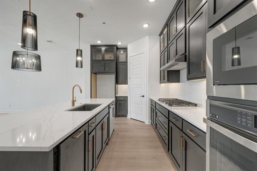 Gourmet kitchen featuring an oversized island with an undermount sink and gold-finish faucet, dark cabinetry, and light wood-finish flooring Gourmet kitchen featuring an oversized island with an undermount sink and gold-finish faucet, dark cabinetry, and light wood-finish flooring