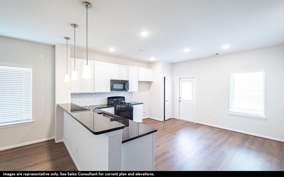 Kitchen with tasteful backsplash, white cabinets, black appliances, wood finished floors, and dark countertops