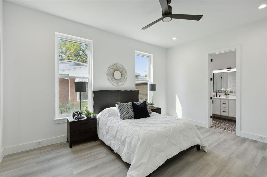 Bedroom with ceiling fan, light wood-type flooring, ensuite bath, and multiple windows