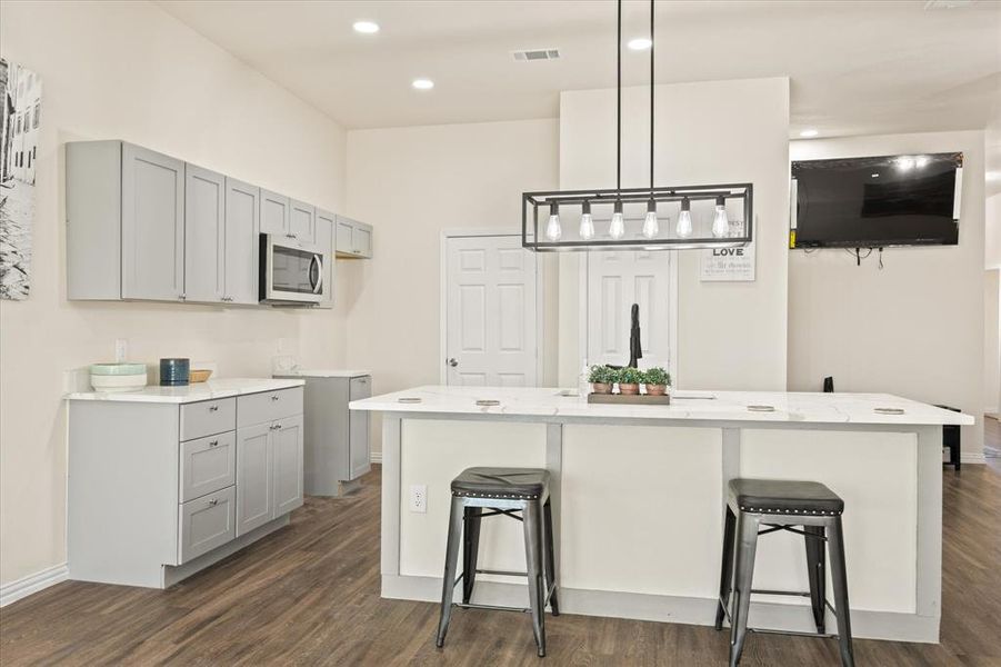 Kitchen featuring pendant lighting, gray cabinets, a breakfast bar area, and an island with sink