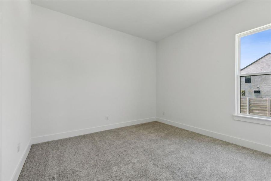 Neutral-toned room featuring a large window, plush gray carpeting, and crisp white baseboards Neutral-toned room featuring a large window, plush gray carpeting, and crisp white baseboards
