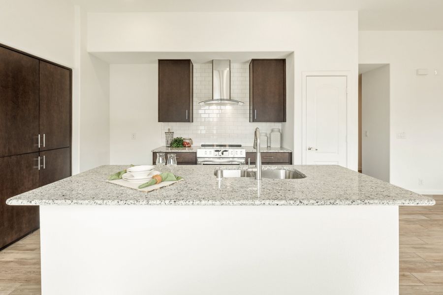Kitchen with granite island sink, dark wood cabinets, white subway tile backsplash, and stainless steel range hood