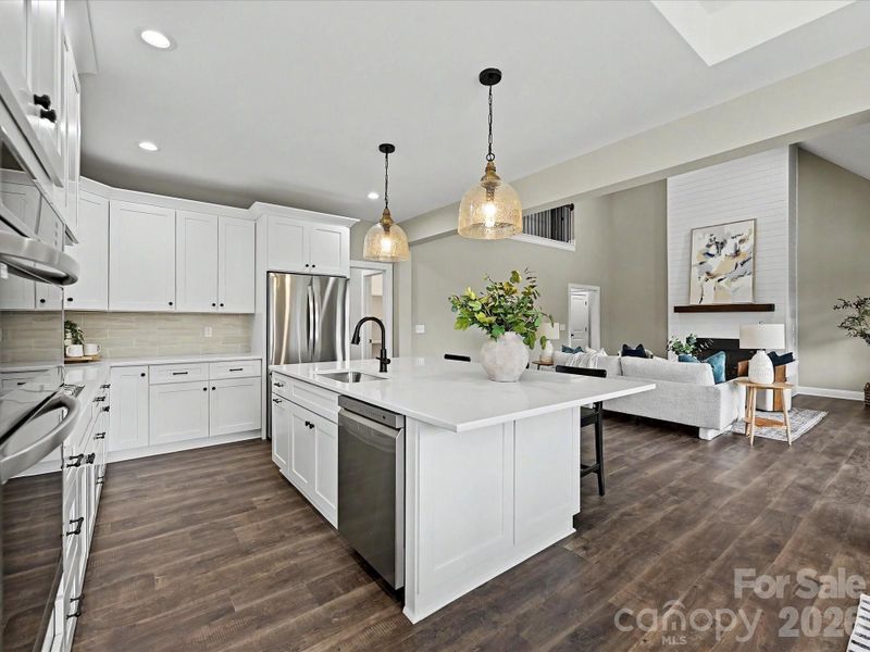 Bright and beautifully designed, this chef’s kitchen features quartz countertops, custom white cabinetry, stainless steel appliances, and a large center island overlooking the open-concept living space.