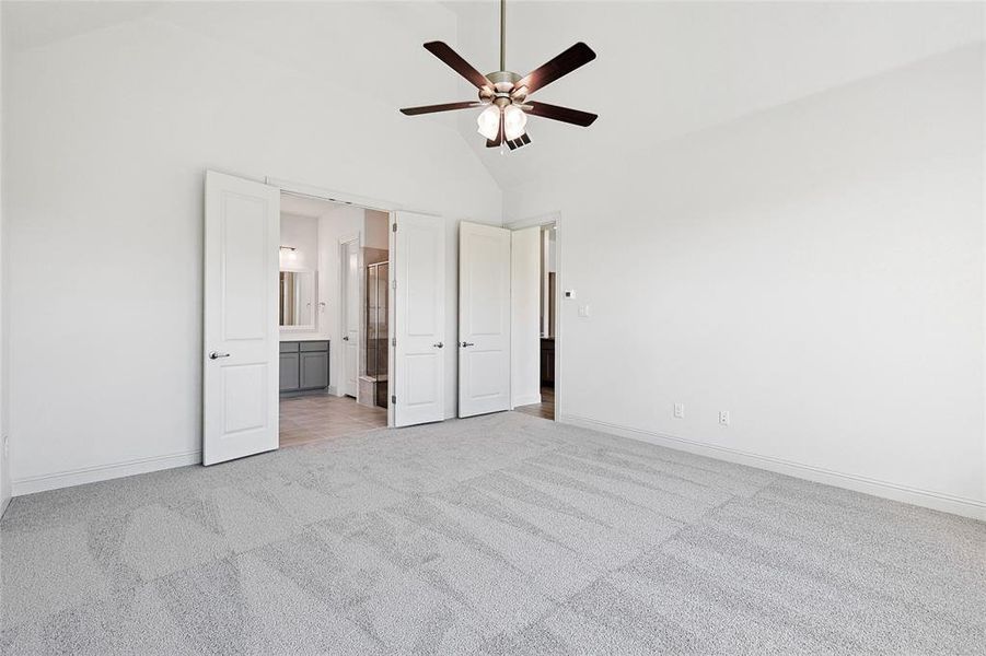 Unfurnished bedroom featuring light carpet, ceiling fan, vaulted ceiling, and ensuite bathroom