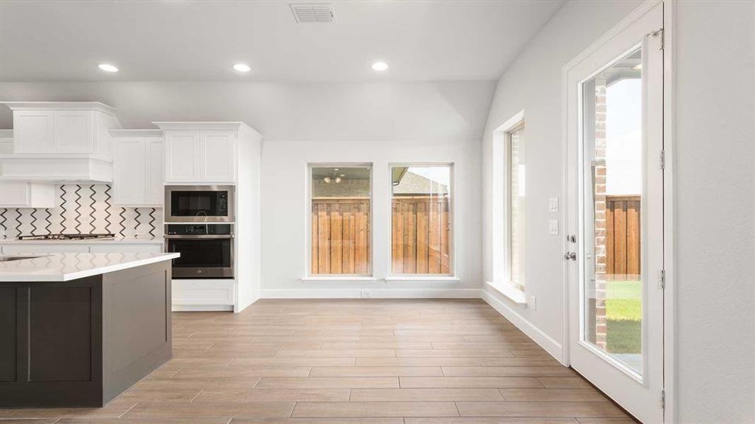 Kitchen featuring built in microwave, oven, light hardwood / wood-style flooring, light stone countertops, and white cabinetry