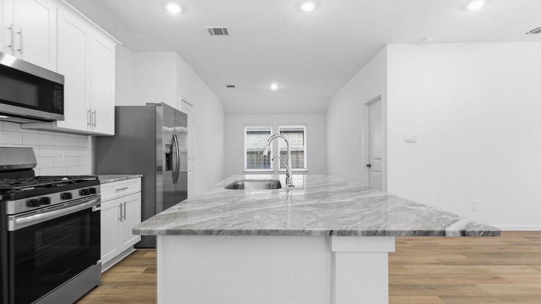 Bright and spacious kitchen with granite countertops, stainless steel appliances, and an island with bar seating.