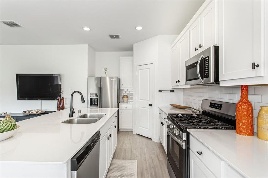 The kitchen features white cabinetry, stainless steel appliances, a double basin sink, and a white subway tile backsplash