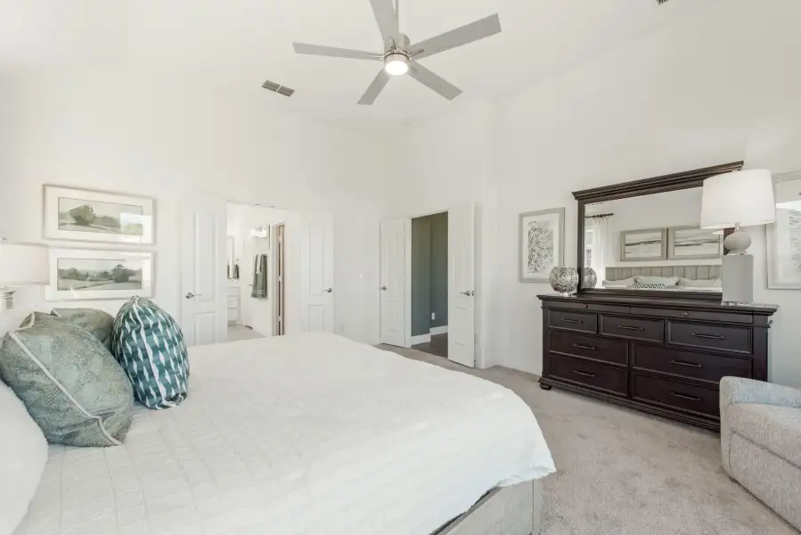 Master bedroom with high ceilings, ceiling fan, dark wood dresser, and doors leading to bathroom and closet
