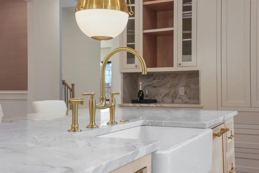 Kitchen island featuring a white apron sink, a gold-toned faucet, and a light-colored countertop with visible veining