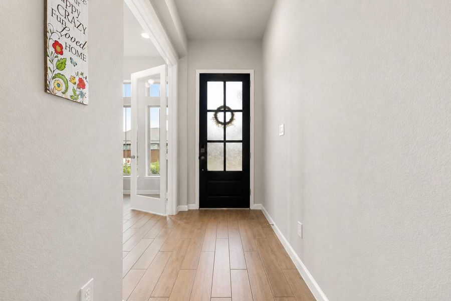 Welcoming entryway with elegant wood-look tile flooring and modern front door leading into the private home office on the right.