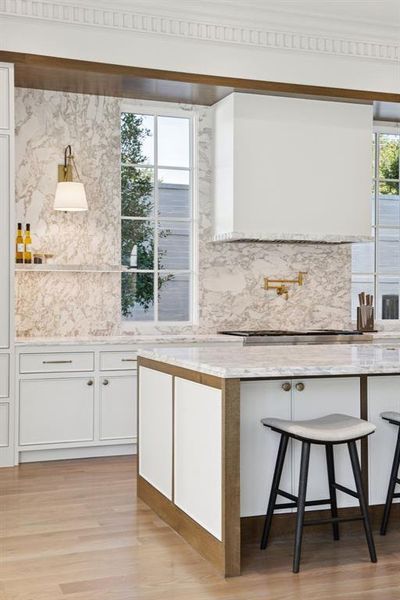 Kitchen featuring white cabinetry, a kitchen bar, light wood-style flooring, and light stone countertops
