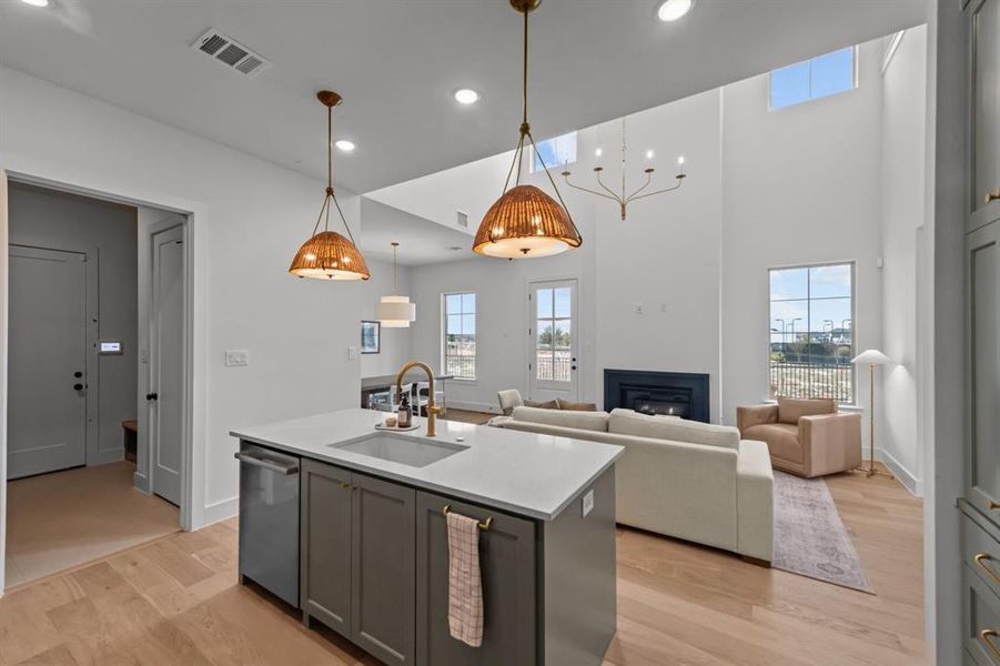 Kitchen featuring sink, stainless steel dishwasher, gray cabinets, an island with sink, and pendant lighting