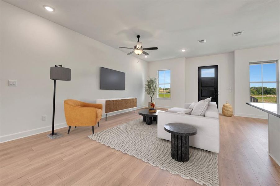 Spacious living area featuring light wood-finish flooring, a contemporary ceiling fan with integrated lighting, and recessed ceiling lights Spacious living area featuring light wood-finish flooring, a contemporary ceiling fan with integrated lighting, and recessed ceiling lights