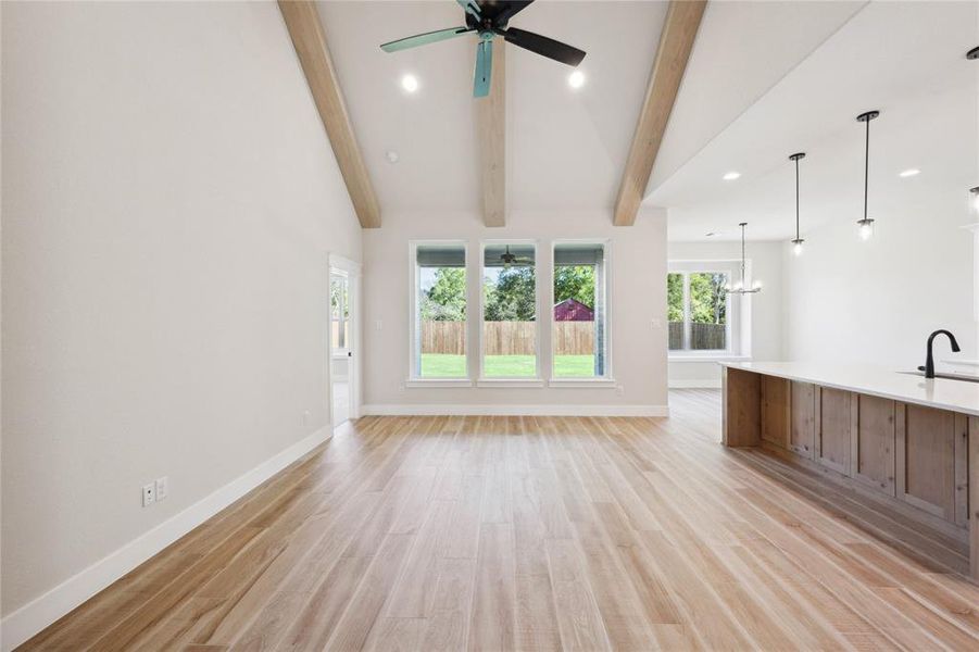 Unfurnished living room with light wood-type flooring, ceiling fan with notable chandelier, sink, beam ceiling, and high vaulted ceiling