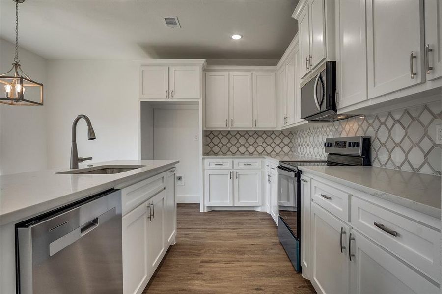 Kitchen with appliances with stainless steel finishes, decorative backsplash, dark wood finished floors, white cabinets, and recessed lighting Kitchen with appliances with stainless steel finishes, decorative backsplash, dark wood finished floors, white cabinets, and recessed lighting