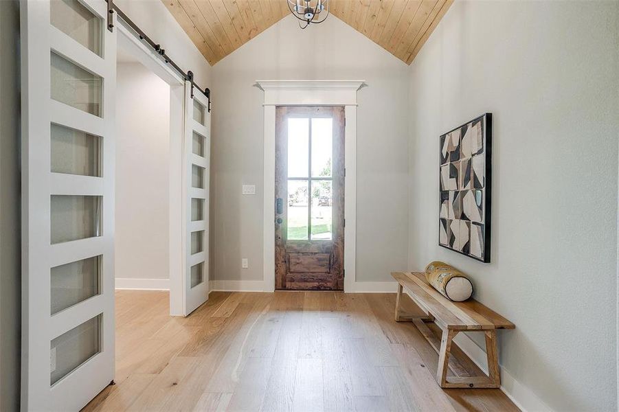 Foyer entrance with a barn door, wood ceiling, light wood finished floors, baseboards, and lofted ceiling Foyer entrance with a barn door, wood ceiling, light wood finished floors, baseboards, and lofted ceiling