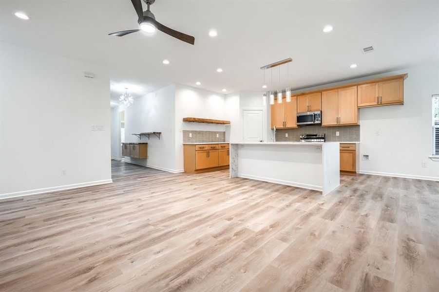 Kitchen with open floor plan, backsplash, an island with sink, light wood-style flooring, and recessed lighting