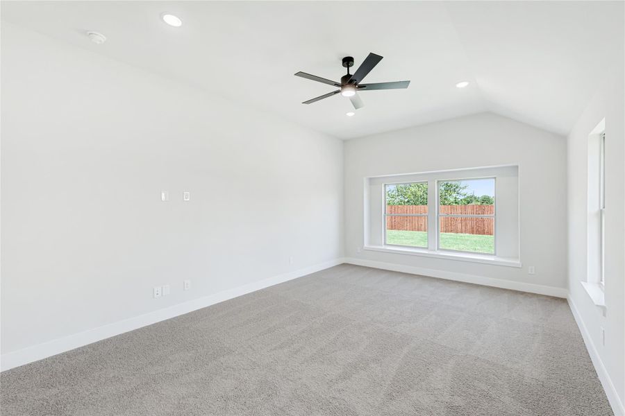 Empty bedroom with vaulted ceiling, ceiling fan, carpet flooring, and backyard-facing window